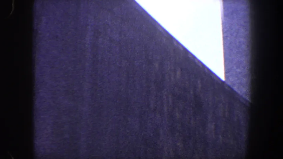 1960 New York City home-movie frame showing a low-angle view of a tall modernist facade with a bright sky opening above.