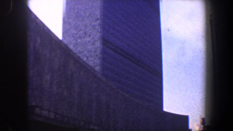 1960 New York City frame with angular high-rise surfaces, a bright sky gap and a dark rail-like line along the lower edge.