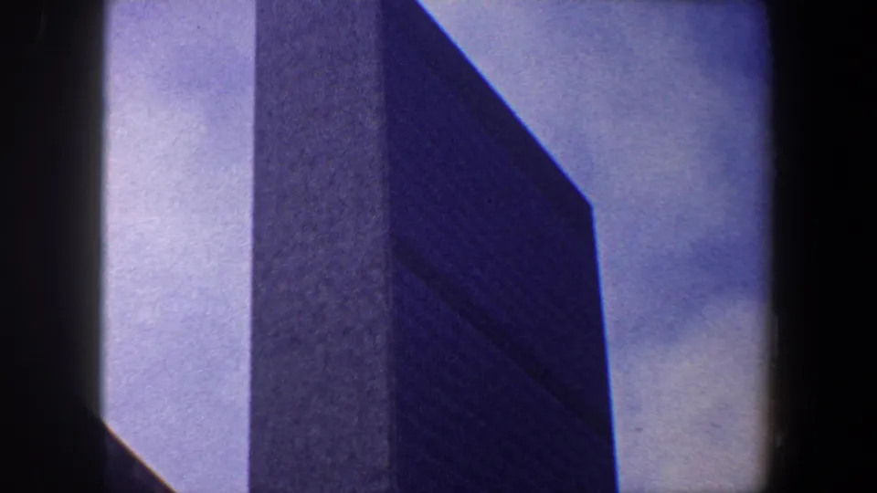 1960 New York City 8mm frame showing a tall dark skyscraper rising against a pale blue sky.