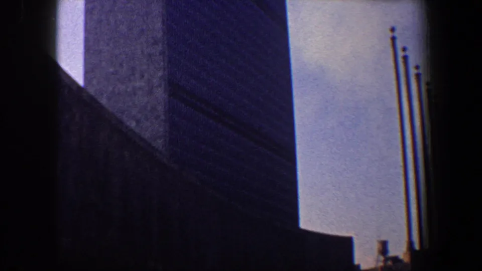 The 1960 New York City 8mm shot pans down to reveal flagpoles beside the lower section of the skyscraper.