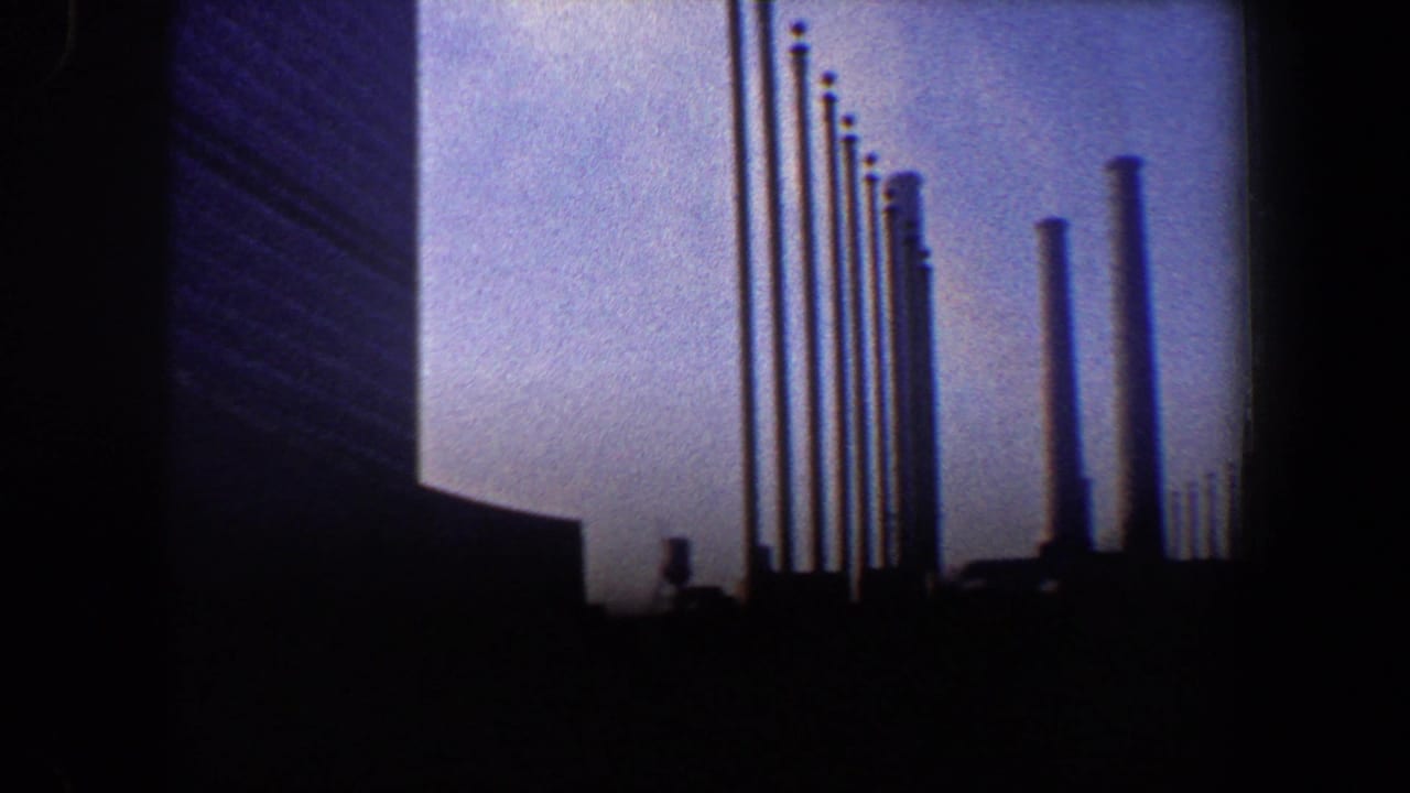 Tall building edge with rows of flagpoles silhouetted against pale sky.