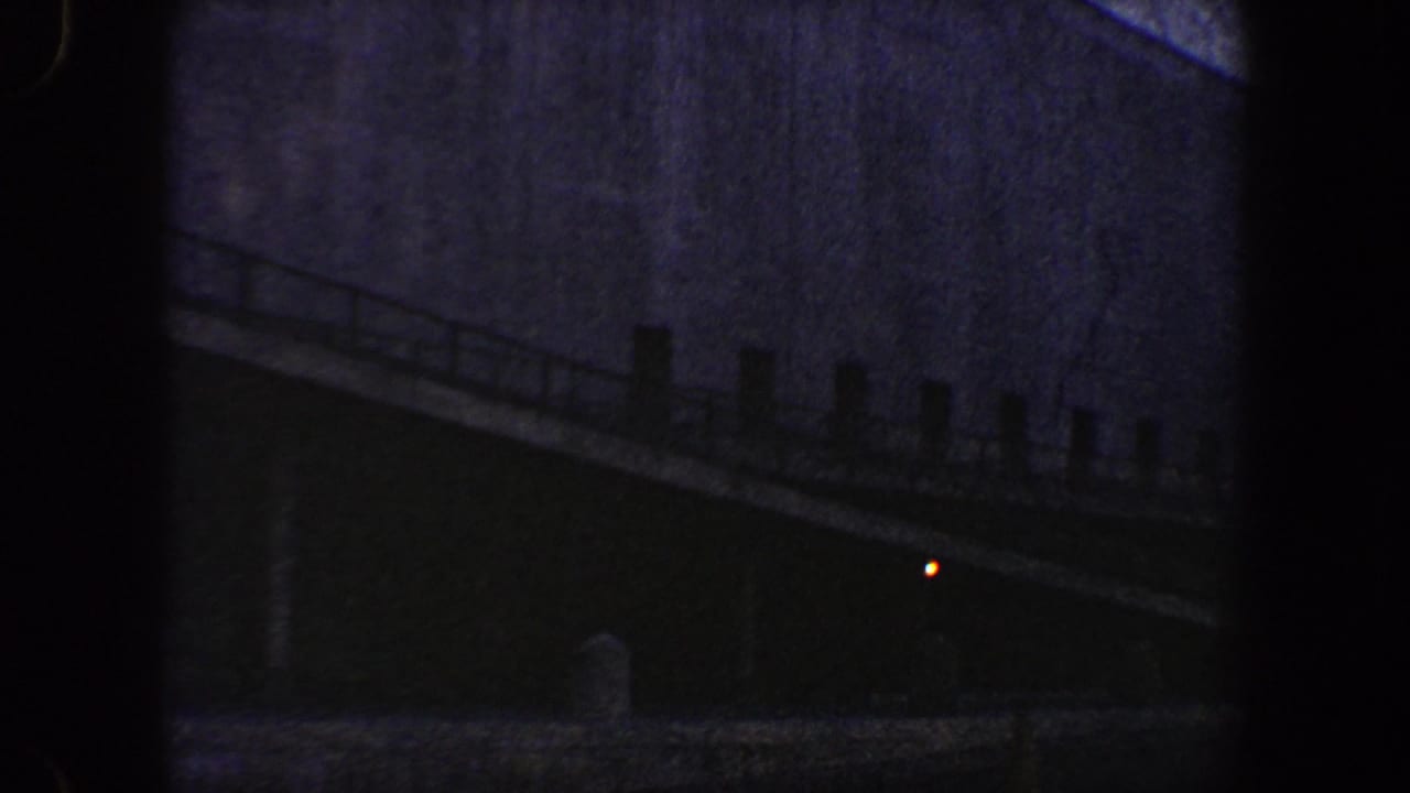 Dark sloped walkway or ramp with railing beside a large building wall.