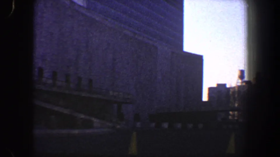 1960 New York City exterior frame with a large shadowed wall, sloped railing, dark foreground, and bright sky between buildings.