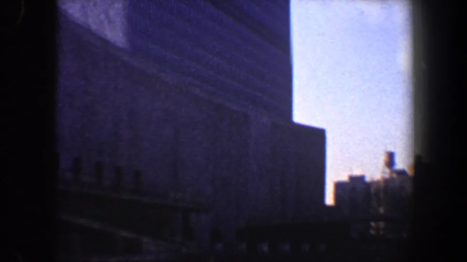 1960 New York City 8mm frame showing shadowed skyscraper facades, narrow sky openings, and a dark foreground edge.