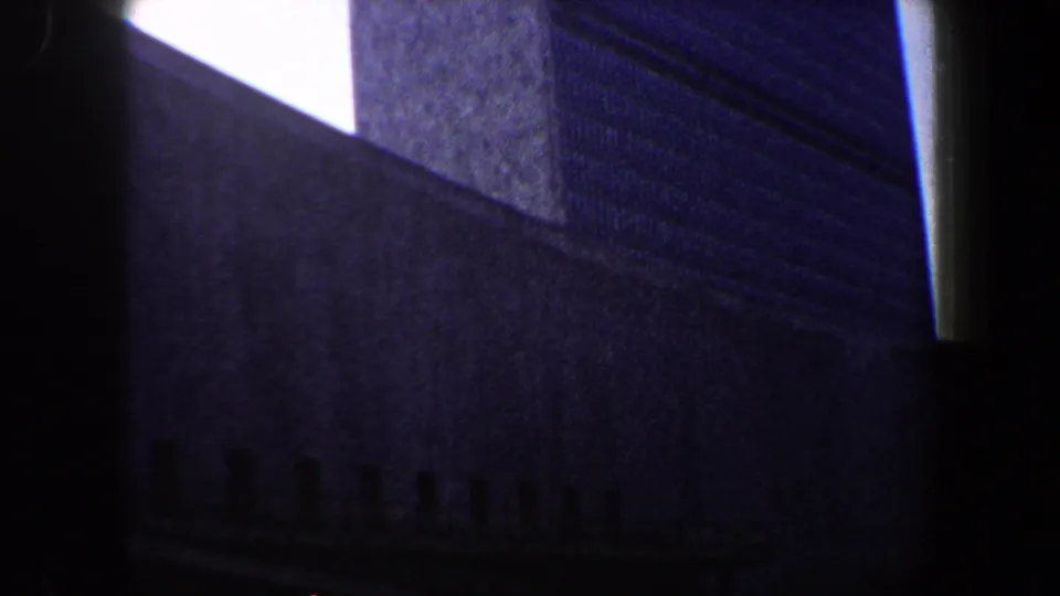 1960 New York City 8mm frame showing a steep high-rise facade, bright sky wedge, and dark lower architectural silhouettes.