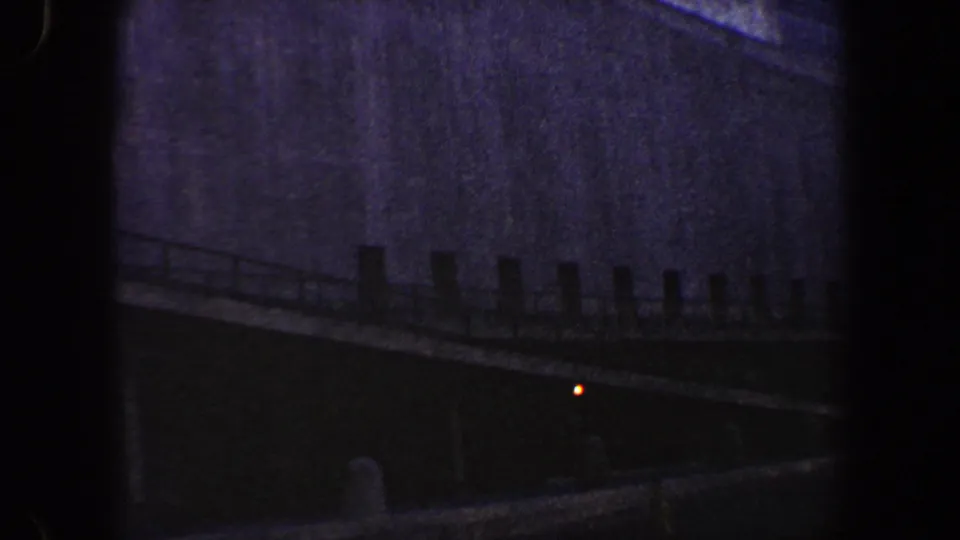 1960 New York City 8mm frame showing a dark building exterior, lower ledge or roofline, and a small orange light in shadow.