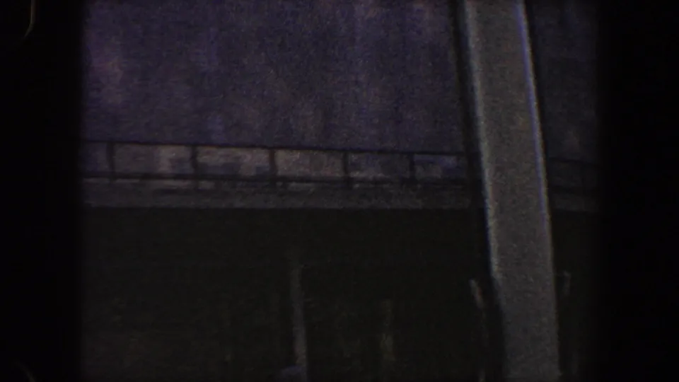Underexposed 1960 New York City 8mm frame showing a dark commercial facade, railing, and heavy vertical foreground shadow.
