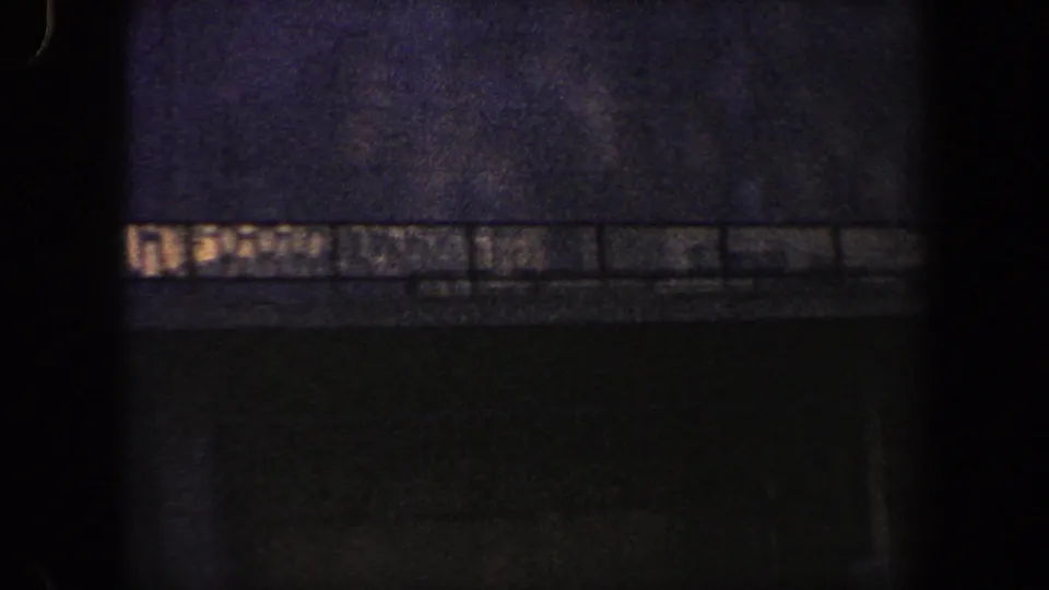 Grainy 1960 New York City frame with a dark commercial facade, railing, and an indistinct illuminated band on the building.