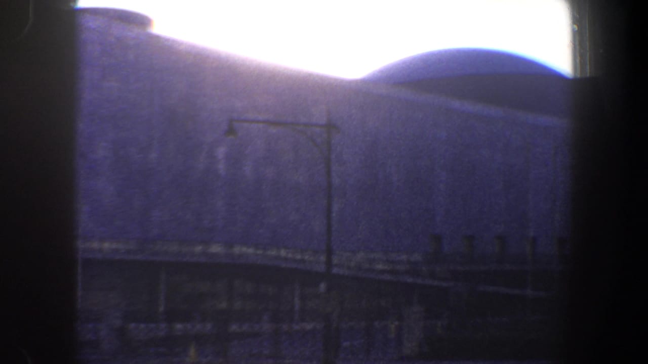 1960 New York City frame of a large building with a rounded roof form and streetlamp in the foreground, with dark vertical window framing crossing the view.