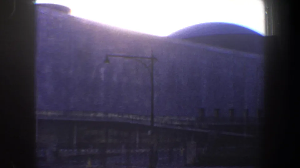 1960 New York City frame of a large building with a rounded roof form and streetlamp in the foreground, with dark vertical window framing crossing the view.