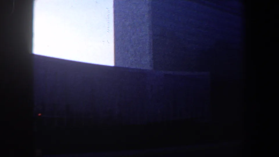 1960 New York City 8mm frame showing a tall building facade from below, with bright sky and deep street-level shadow.