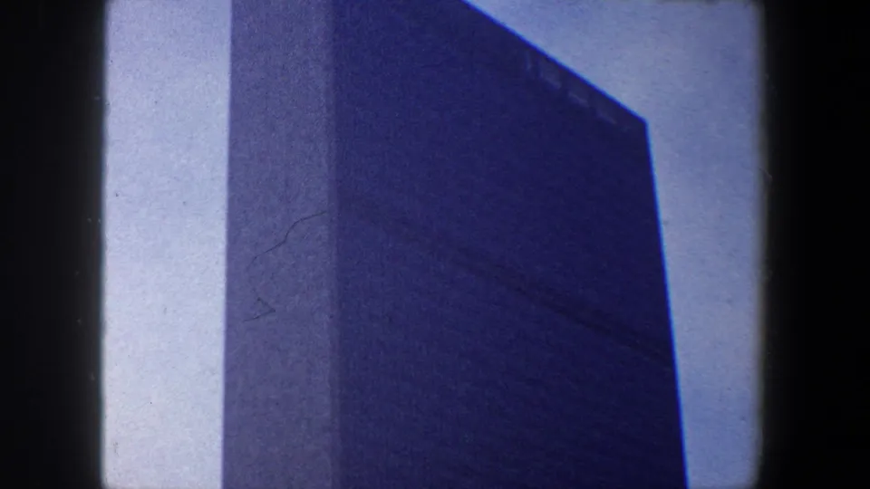 1960 New York City home-movie frame showing the United Nations Headquarters tower from below, with dark 8mm film borders.