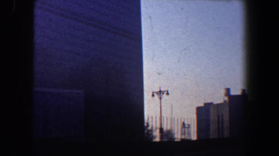 1960 New York City frame showing United Nations Headquarters with streetlights, fence-like verticals, and surrounding urban silhouettes.
