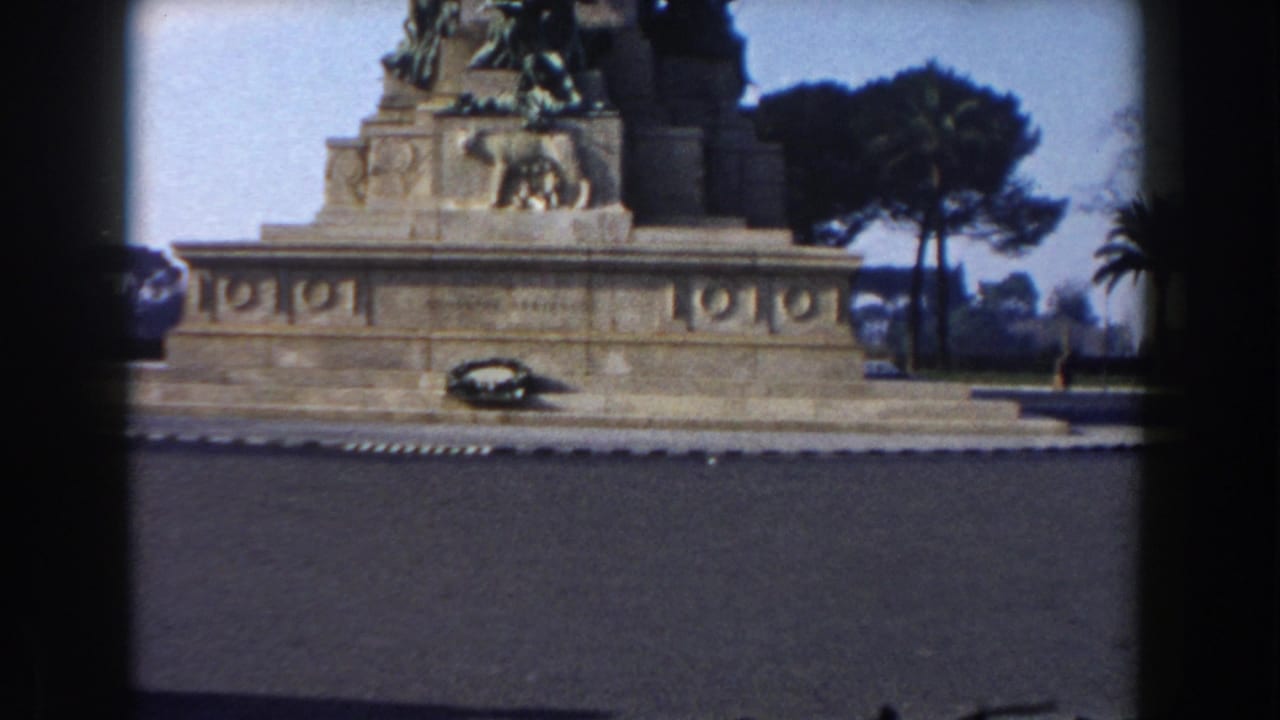 Monument pedestal and bronze sculpture framed by trees, with dark film gate edges.