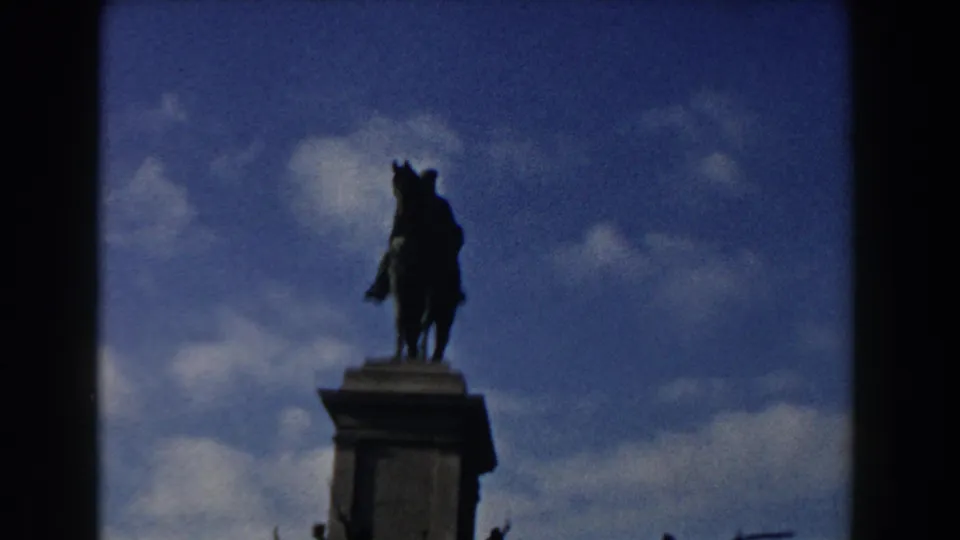 1959 Rome 8mm frame showing a tighter low-angle view of the equestrian statue and pedestal top with soft focus and grain.