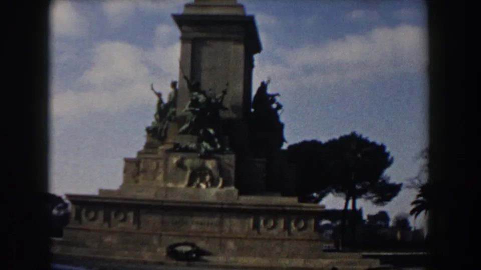 Rome travel footage frame showing the monument base, bronze figures, pedestal, trees, and open sky.