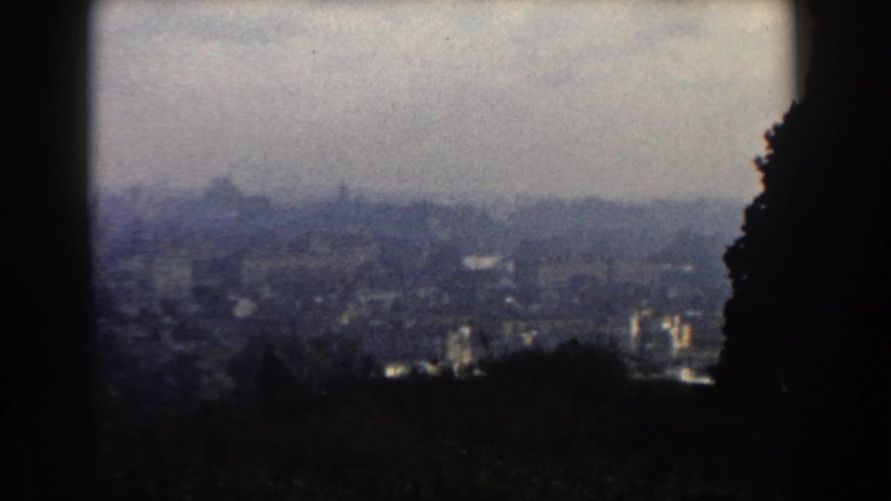 1959 8mm view of Rome from surrounding hills, showing a hazy skyline framed by dark foreground shapes.