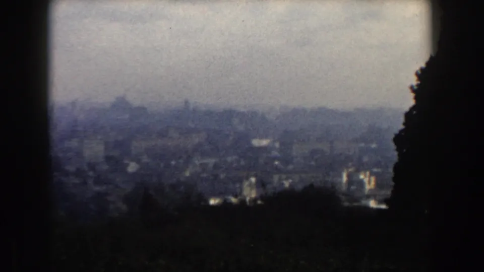 1959 8mm view of Rome from surrounding hills, showing a hazy skyline framed by dark foreground shapes.