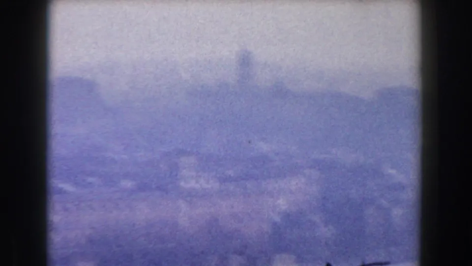 Blue-shifted 8mm frame of Rome in 1959, with a soft skyline and indistinct urban forms under haze.