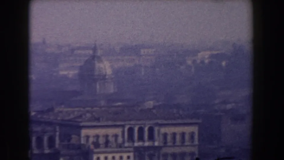 A Rome skyline frame from 1959 shows a dome and pale foreground facade softened by haze and film grain.