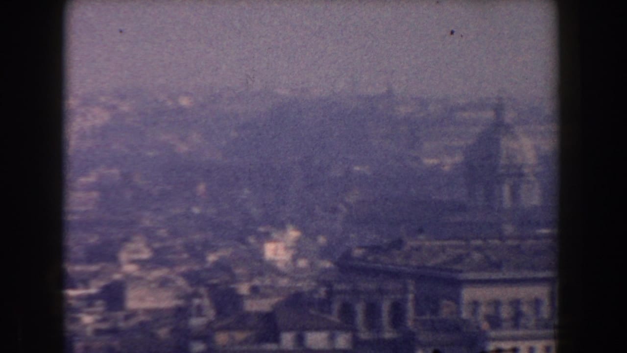 1959 8mm view over Rome with rooftops and a large historic building softened by haze and film grain.