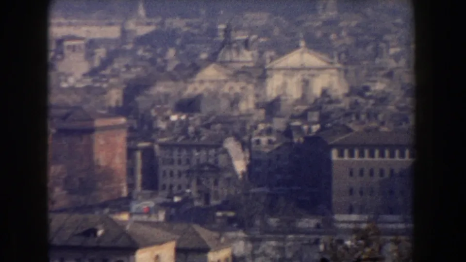 1959 8mm Rome overlook with a pale church-like facade, domes, rooftops, and dark frame bars at the edge.