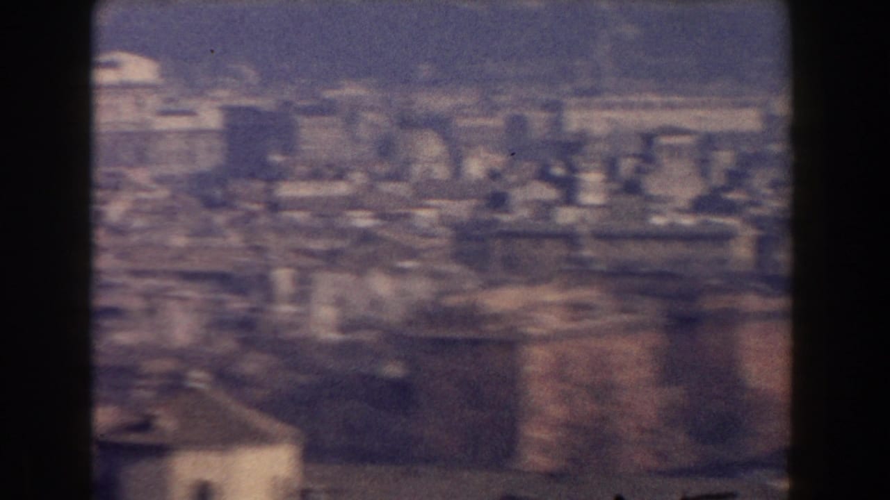 1959 Rome home-movie aerial view with clustered rooftops, tall buildings, haze, and visible 8mm frame edges.