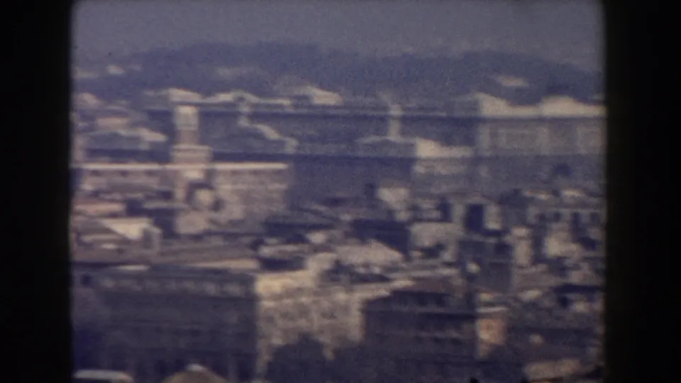 1959 Rome aerial frame showing historic urban blocks, a prominent pale building, haze, and distant hills.