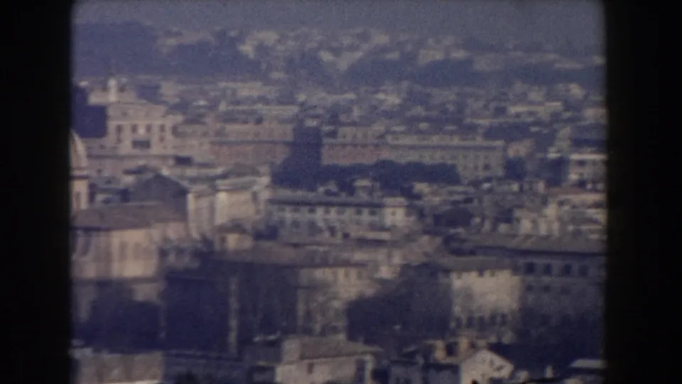 1959 Rome home-movie view across layered rooftops, masonry buildings, trees, and a softly rendered skyline.