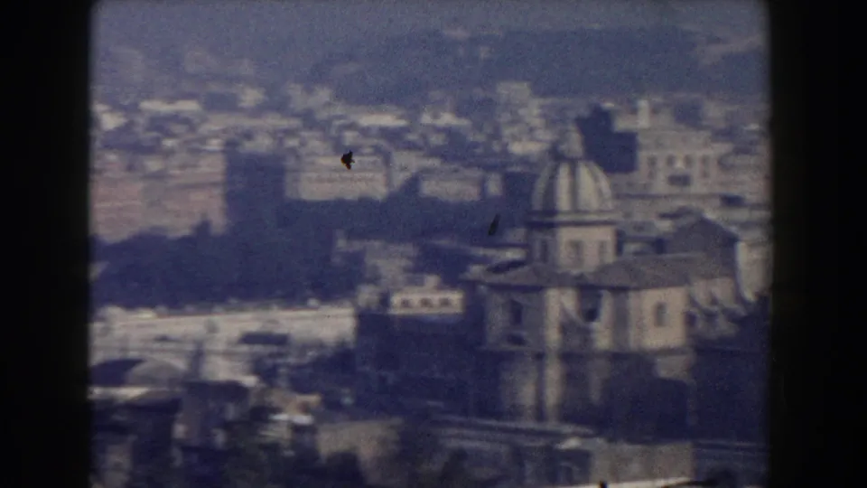 1959 Rome aerial frame with a domed church-like structure, nearby rooftops, distant buildings, and hills.