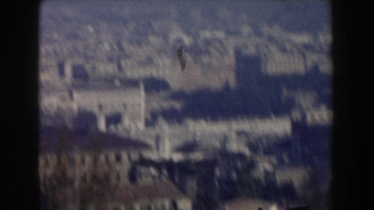 1959 8mm home-movie frame showing a blurred elevated view across Rome buildings, treetops and hazy sky.