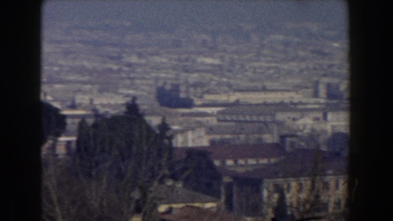 Rome cityscape in a 1959 8mm frame, with low buildings, dark trees in the foreground and a hazy distant horizon.