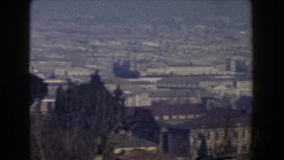 Rome cityscape in a 1959 8mm frame, with low buildings, dark trees in the foreground and a hazy distant horizon.