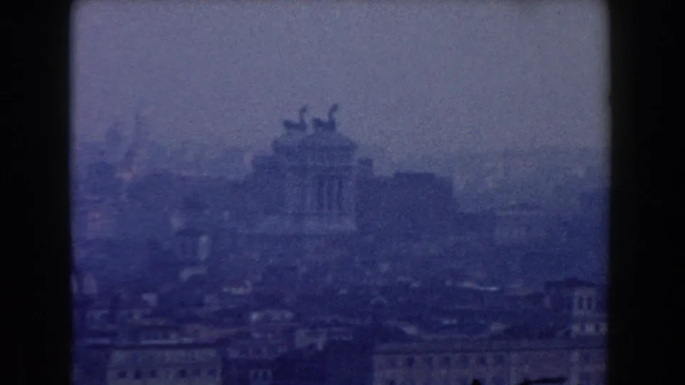Blue-tinted 1959 8mm frame showing Rome from above with the Altare della Patria centered in haze.