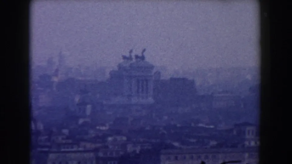 Soft 8mm view of the Altare della Patria and surrounding Rome buildings under a pale, hazy sky.