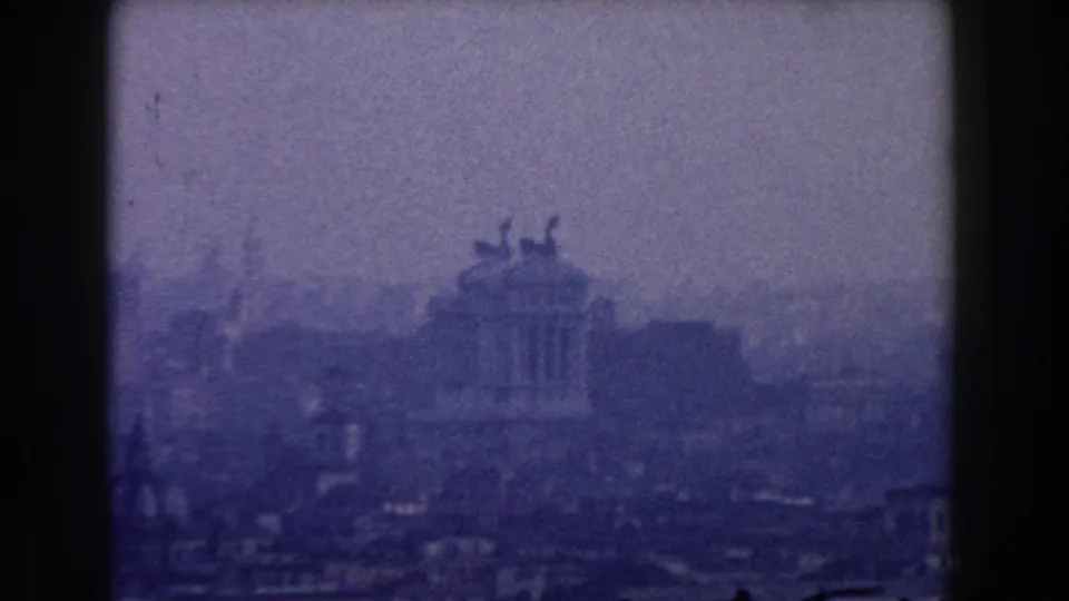 Blue-violet 8mm frame of Rome in 1959, with the Altare della Patria softened by haze and grain.