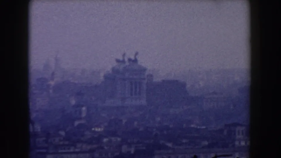 Late-1950s 8mm view of the Altare della Patria across dense Rome rooftops, framed by dark film edges.