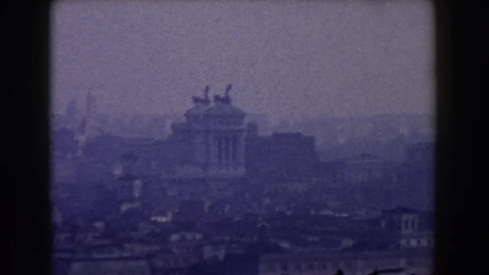 1959 Rome skyline view with the Altare della Patria area appearing through haze, grain, and blue-tinted 8mm exposure.