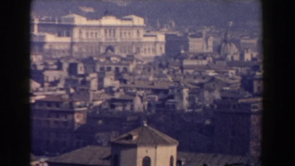 1959 Rome cityscape with layered masonry buildings, a foreground roof, and a bright monumental structure across the skyline.