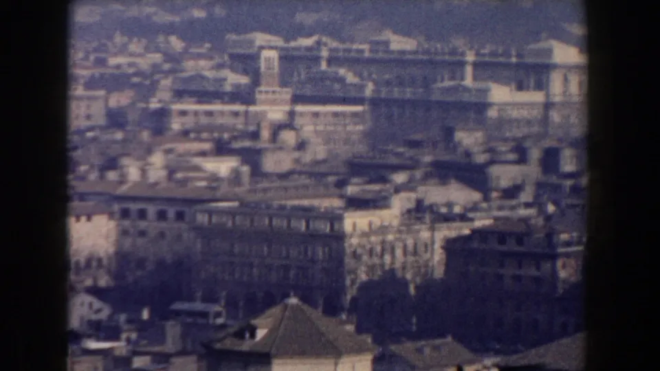 1959 Rome home-movie frame showing an elevated city view with dense buildings and a large historic structure beyond.