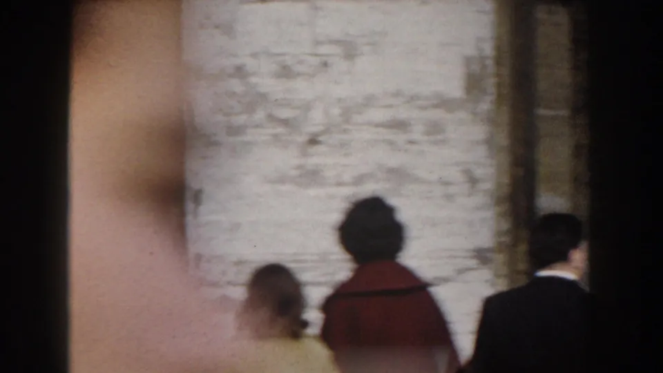 Rome church exterior in 1959 with people walking past a pale stone wall, partly obscured by handheld framing.