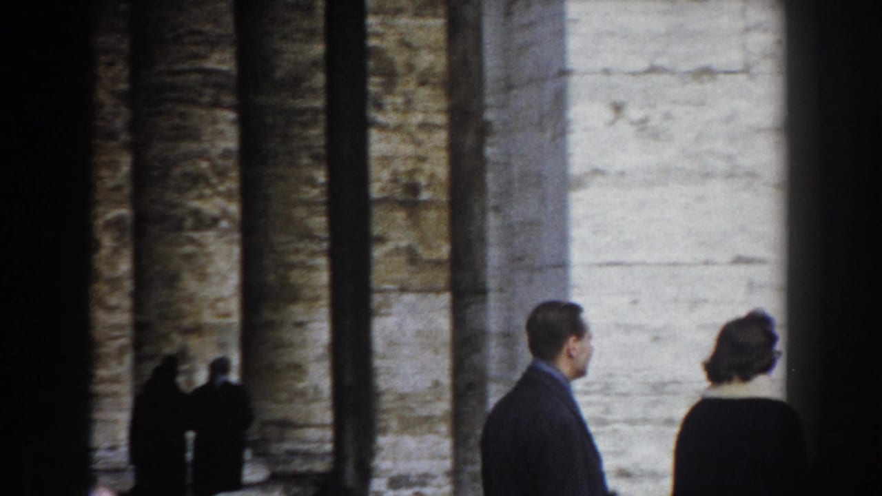 Rome 1959 home-movie frame showing visitors beside large stone columns, with more people gathered in the background.