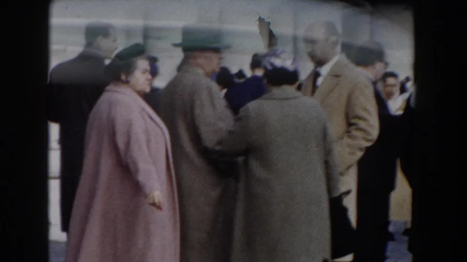 Rome 1959 crowd scene with adults in mid-century coats and hats standing before a historic stone colonnade.