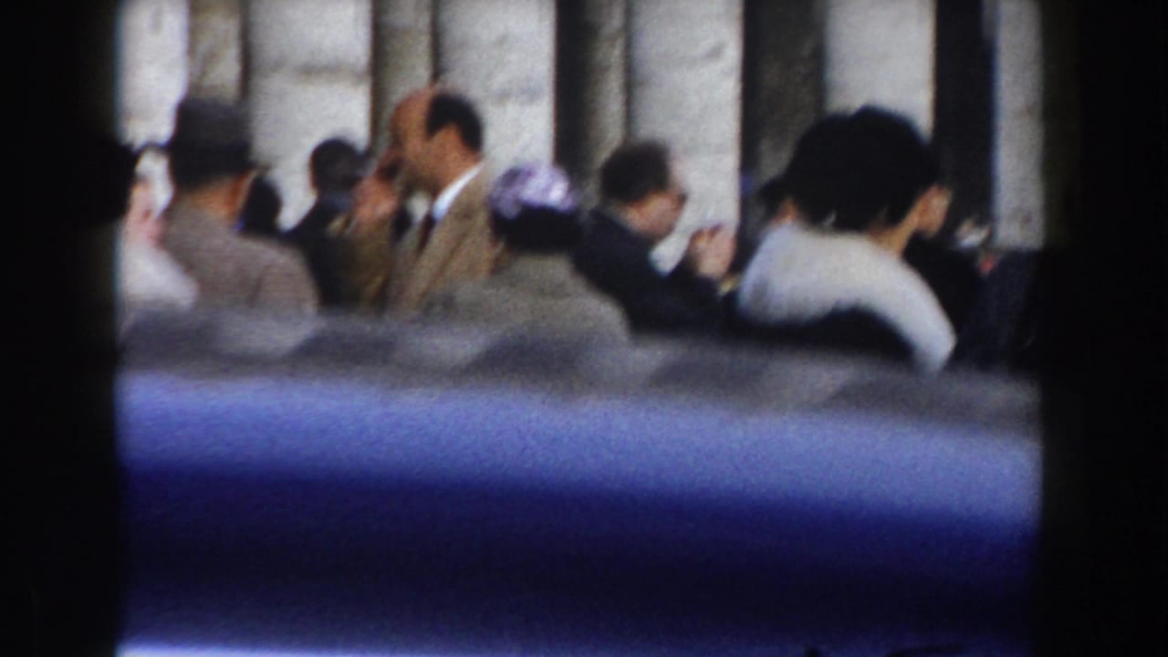 1959 Rome home-movie frame showing formally dressed tourists gathered near a large stone structure.