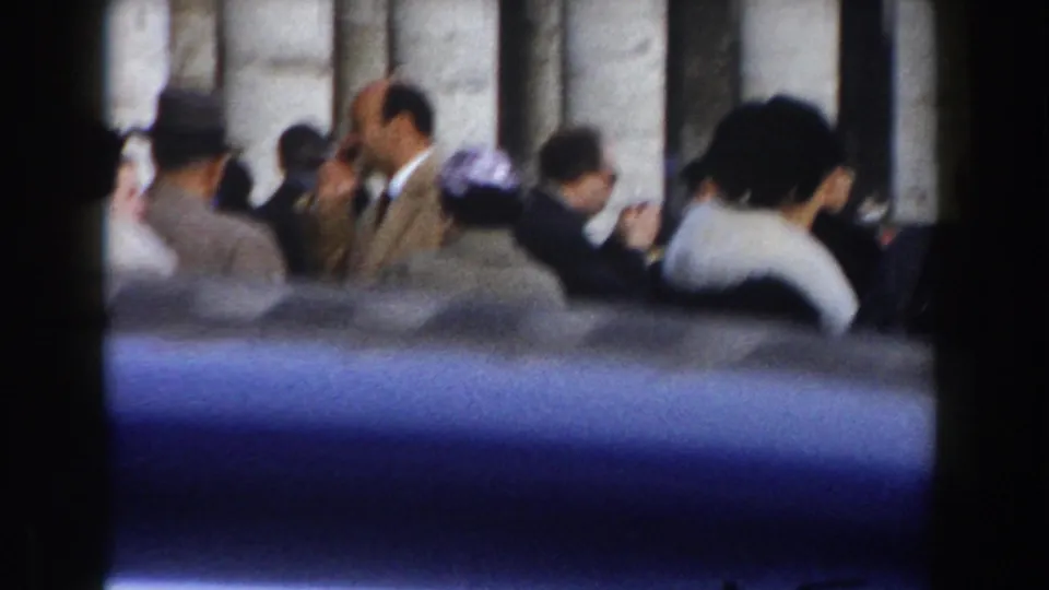 1959 Rome home-movie frame showing formally dressed tourists gathered near a large stone structure.