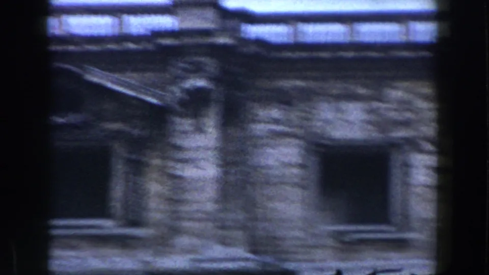 Rome 1959 home-movie frame with a blurred stone facade, dark window openings, and a diagonal roofline or ledge.