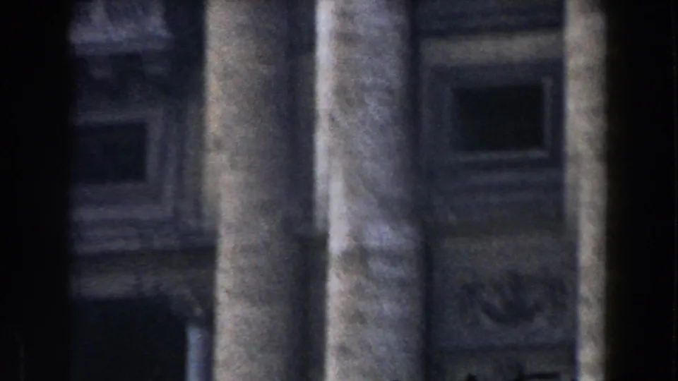 Soft-focus 8mm frame of weathered columns and shadowed stonework at a Roman architectural site.