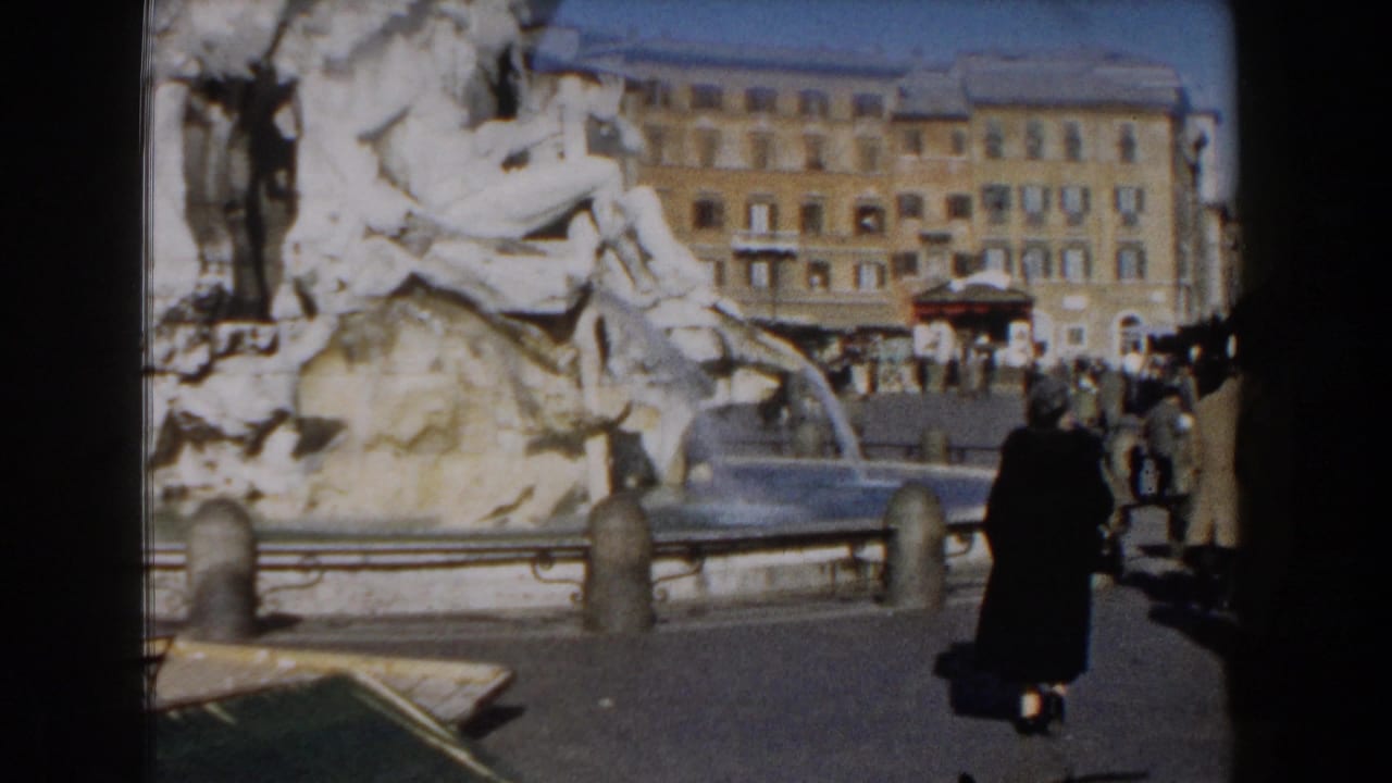 1959 8mm view of the Trevi Fountain in Rome with stone figures, flowing water, pedestrians, and buildings around the piazza.