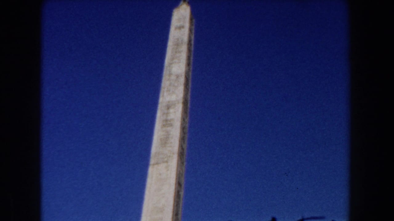 Low-angle view of a pale stone obelisk rising against a deep blue sky.