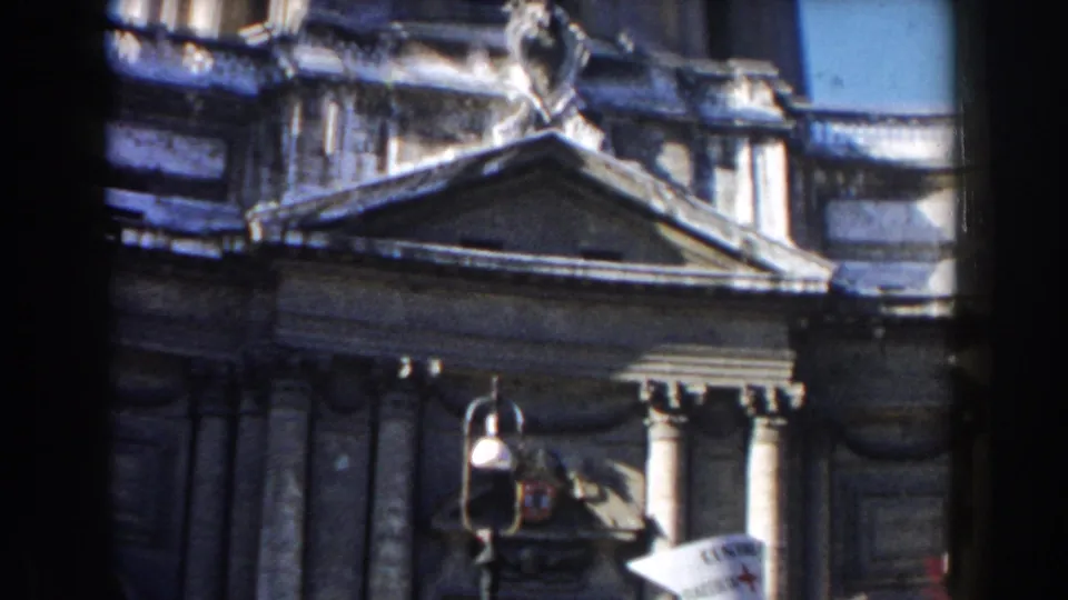 1959 Rome home-movie frame showing a stone facade with columns, triangular pediment, street lamp, and partial dome above.